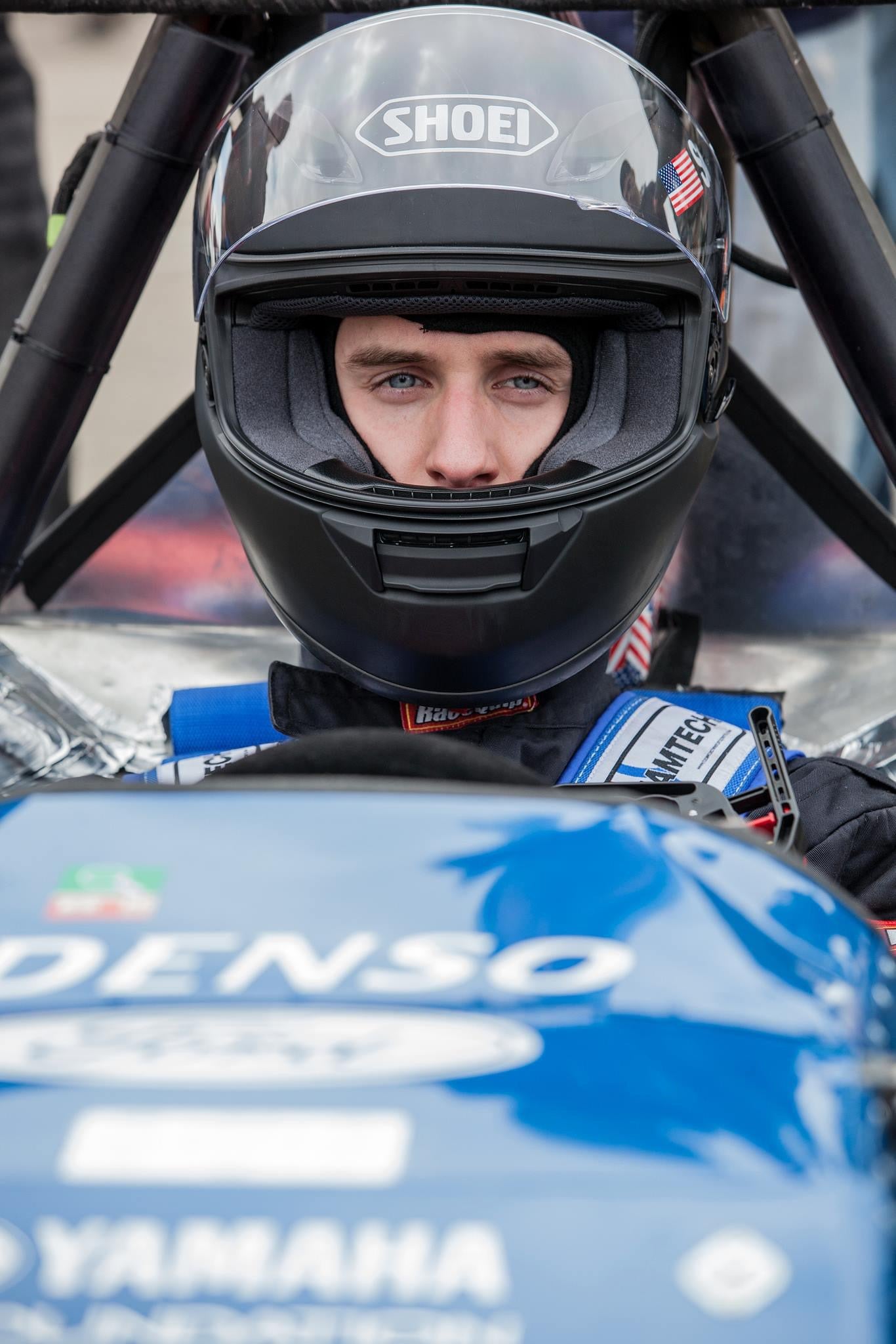 Andrew Smallman with a racecar helmet on, seated in racecar.